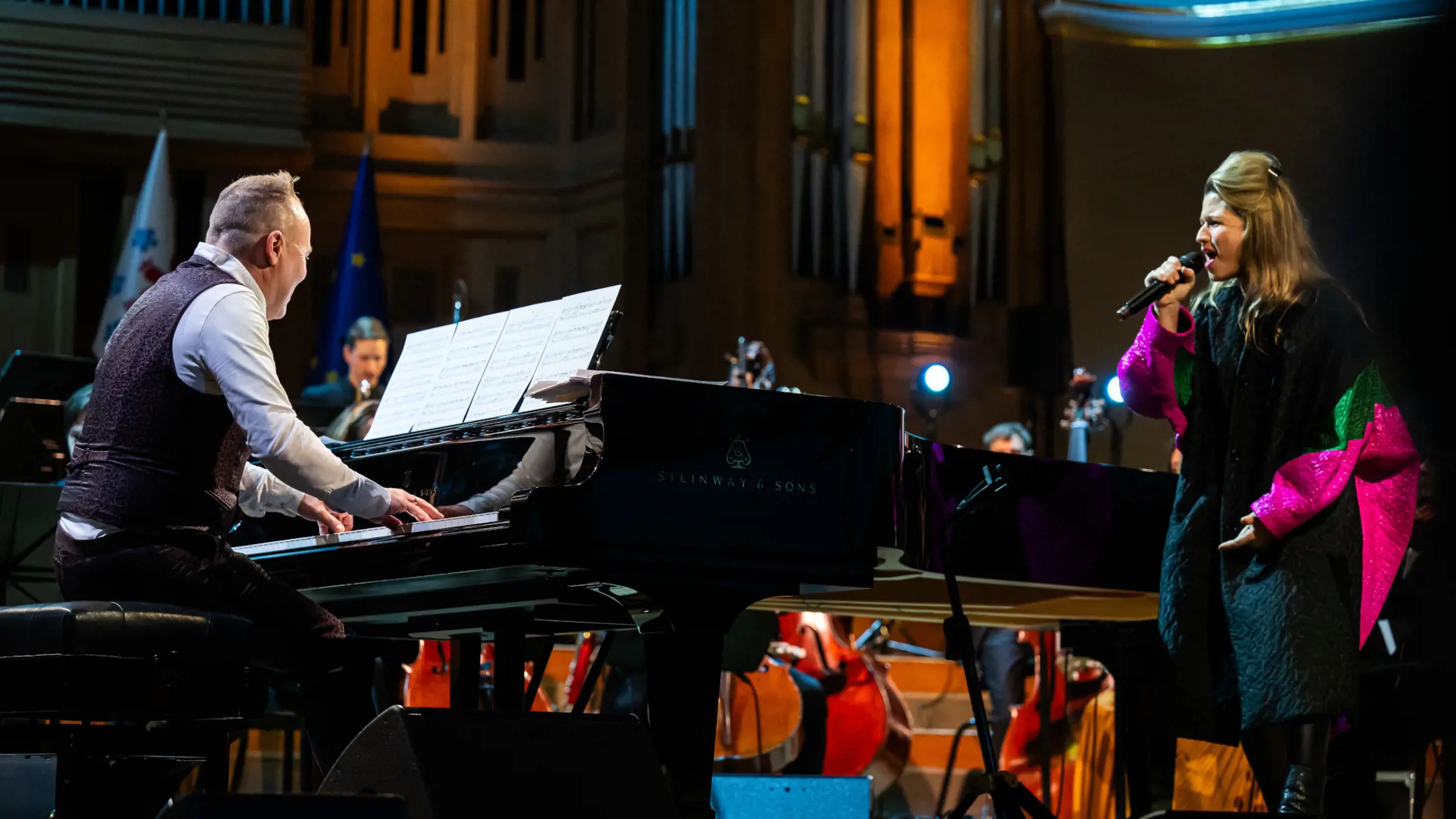 A live shot of two performers in a dark concert house, a man playing a grand piano and a women singing during the concert launching the presidency. Photo credit @ Belgian Presidency.